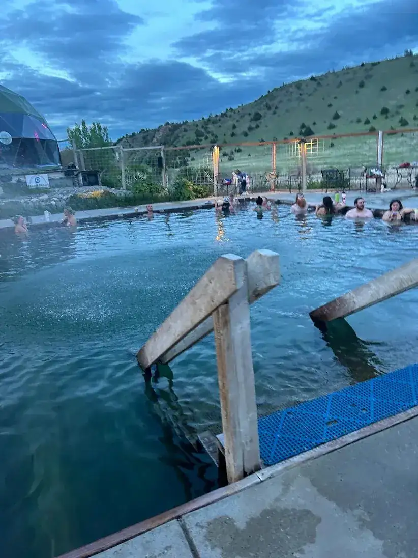 The outdoor pool at Norris Hot Springs at dusk, with the geodesic dome and a grassy hillside behind